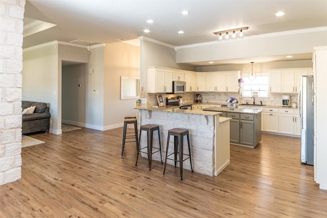 kitchen featuring light stone counters, stainless steel appliances, a peninsula, white cabinetry, and a kitchen breakfast bar