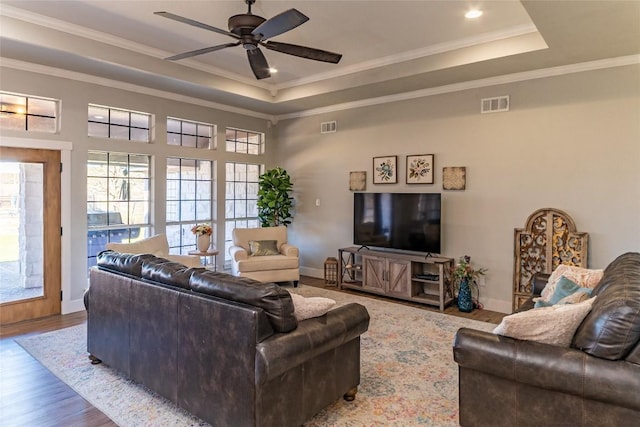 living room with a tray ceiling, wood finished floors, visible vents, and crown molding