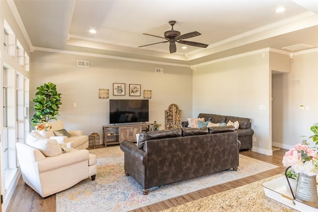 living area featuring light wood-style floors, visible vents, a raised ceiling, and crown molding