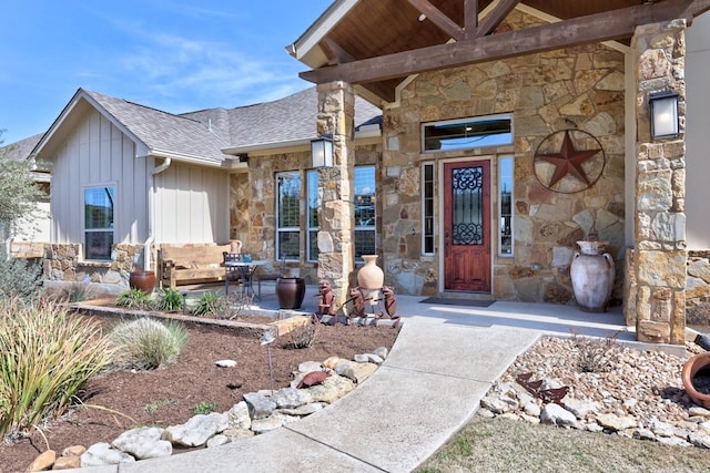 doorway to property featuring board and batten siding, stone siding, and a shingled roof