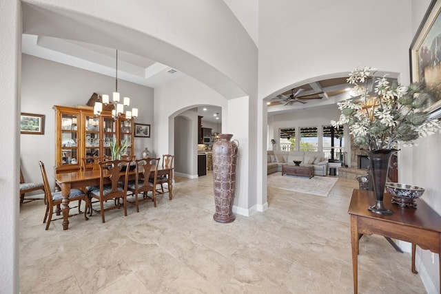 dining room featuring baseboards, visible vents, arched walkways, a towering ceiling, and ceiling fan with notable chandelier