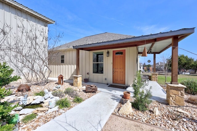 entrance to property featuring a patio, board and batten siding, fence, and roof with shingles