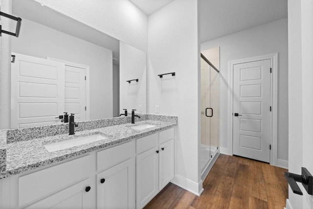 full bath with double vanity, wood finished floors, a stall shower, and a sink