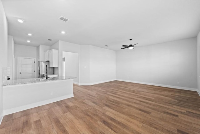 unfurnished living room with ceiling fan, wood finished floors, visible vents, and baseboards