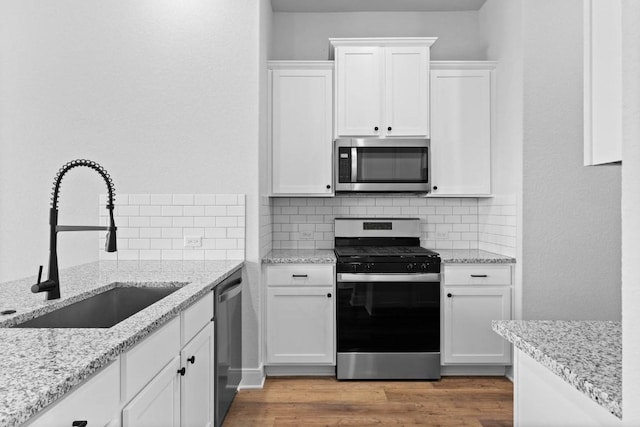 kitchen with appliances with stainless steel finishes, white cabinets, a sink, and light stone counters