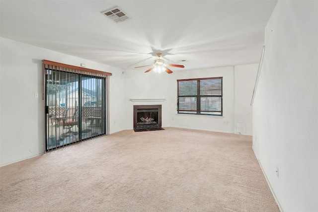 unfurnished living room with a healthy amount of sunlight, a fireplace with flush hearth, visible vents, and light colored carpet