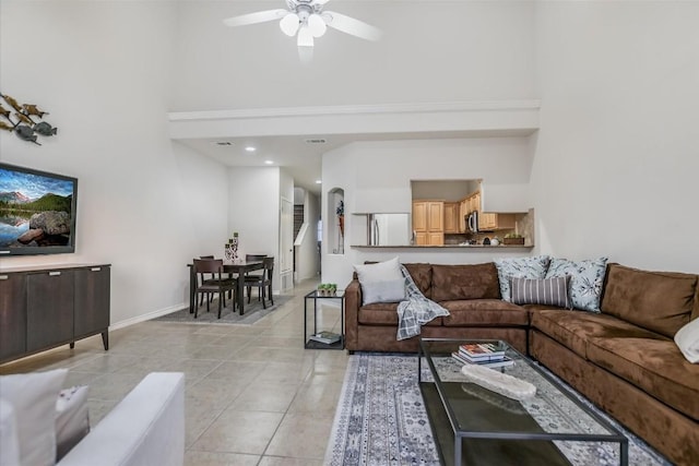 living area with light tile patterned floors, baseboards, a towering ceiling, and a ceiling fan