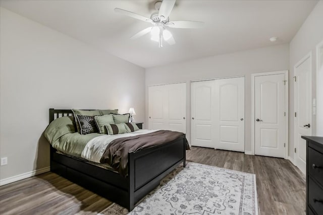 bedroom featuring ceiling fan, wood finished floors, two closets, and baseboards