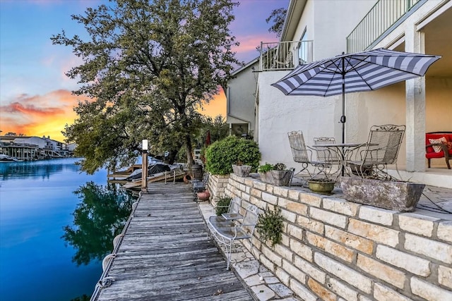 dock area with outdoor dining space, a water view, and a balcony