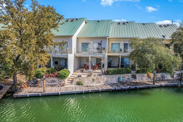 back of property featuring stucco siding, a water view, a patio area, metal roof, and a balcony