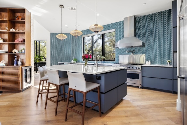 kitchen featuring wallpapered walls, visible vents, high end stainless steel range oven, wall chimney range hood, and a sink