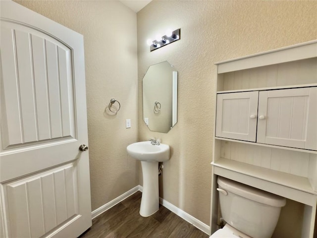 half bathroom featuring toilet, baseboards, wood finished floors, and a textured wall