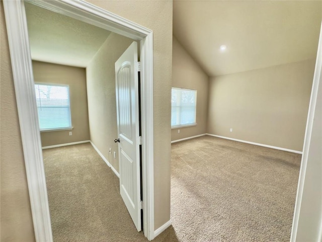 hall with light carpet, baseboards, and lofted ceiling
