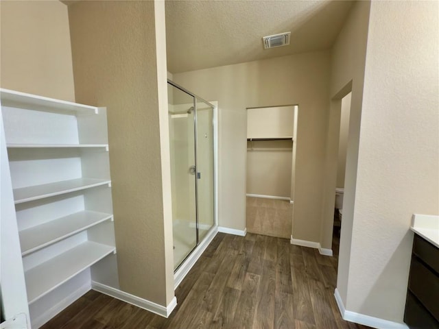 full bathroom with a walk in closet, visible vents, a shower stall, and wood finished floors