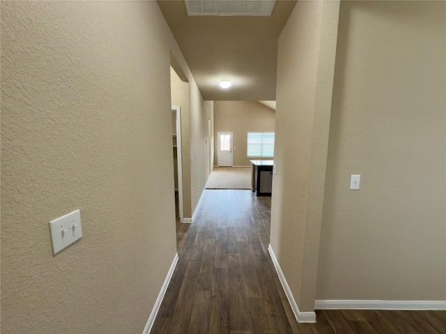 hallway featuring a textured wall, dark wood-style flooring, visible vents, baseboards, and vaulted ceiling