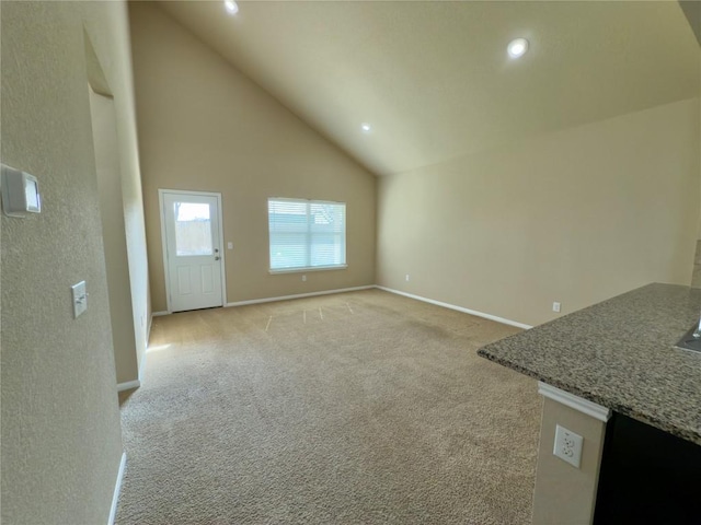 unfurnished living room with high vaulted ceiling, recessed lighting, light colored carpet, and baseboards
