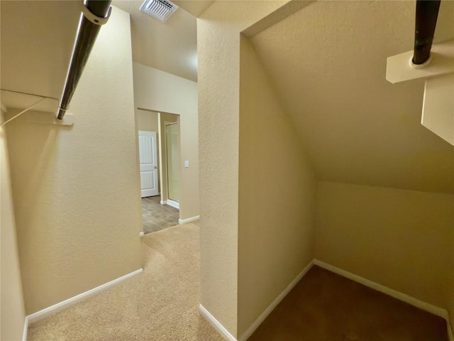 additional living space with baseboards, visible vents, a textured wall, vaulted ceiling, and carpet floors