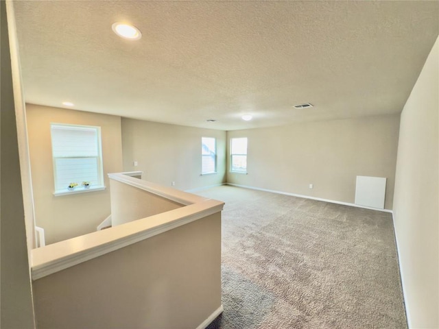 carpeted spare room featuring a textured ceiling, recessed lighting, visible vents, and baseboards