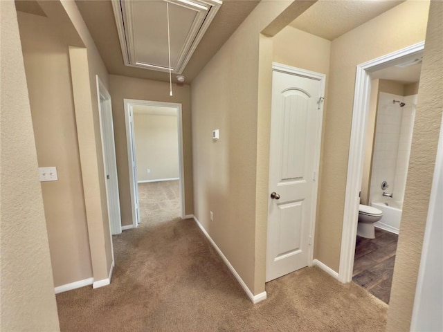 corridor with carpet flooring, attic access, and baseboards