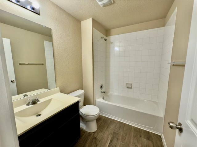 full bath featuring a textured ceiling, a textured wall, toilet, wood finished floors, and washtub / shower combination