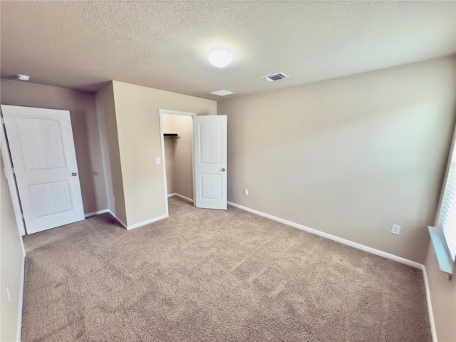 unfurnished bedroom featuring light carpet, baseboards, visible vents, a walk in closet, and a textured ceiling