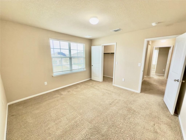 unfurnished bedroom with a textured ceiling, light colored carpet, visible vents, baseboards, and a walk in closet