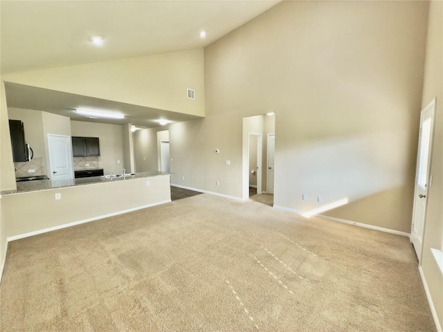 unfurnished living room featuring visible vents, light carpet, a sink, high vaulted ceiling, and baseboards