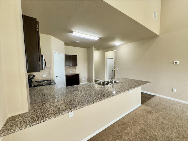 kitchen with light stone counters, dark brown cabinetry, a peninsula, stove, and stainless steel microwave