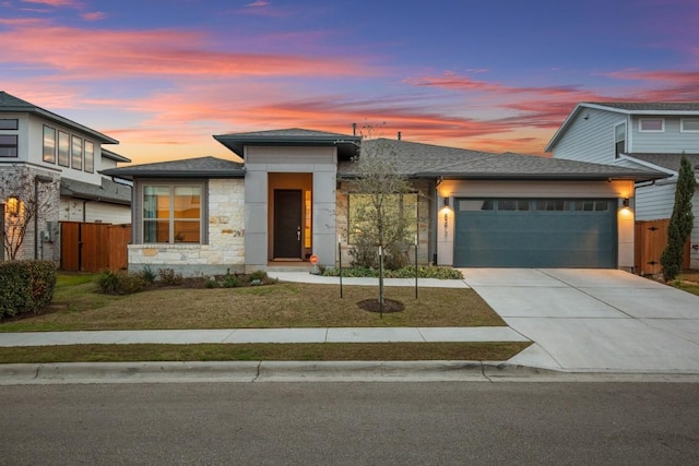 prairie-style house featuring a garage, concrete driveway, stone siding, fence, and a front yard