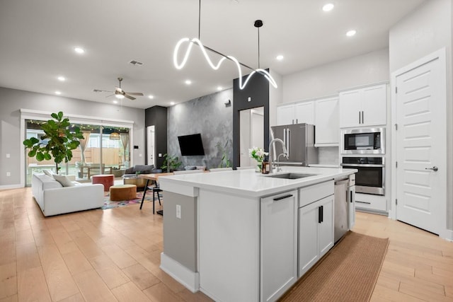 kitchen featuring open floor plan, a kitchen island with sink, stainless steel appliances, light countertops, and white cabinetry