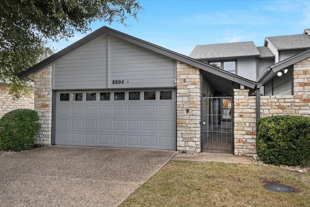 view of front of home featuring a garage, concrete driveway, a shingled roof, and stone siding