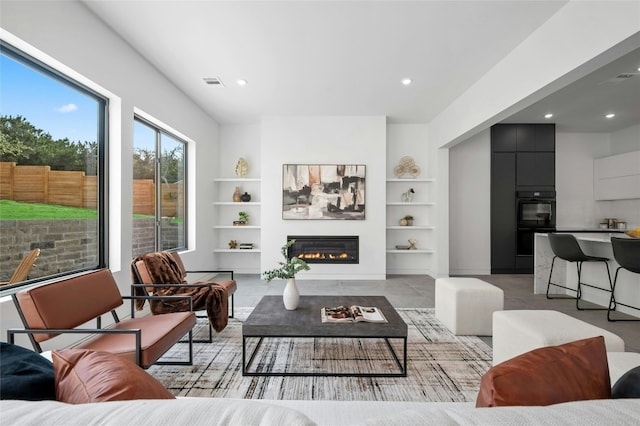 living area featuring recessed lighting, a glass covered fireplace, visible vents, and built in features