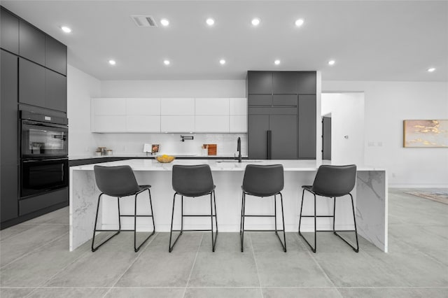 kitchen with dobule oven black, modern cabinets, a breakfast bar, light countertops, and a large island with sink