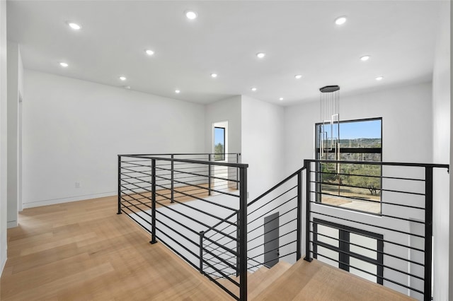 corridor featuring baseboards, light wood-type flooring, an upstairs landing, and recessed lighting