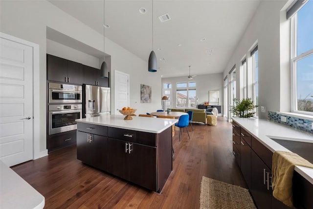 6221 Seville Dr, Austin, TX 78724 - kitchen featuring a kitchen island, open floor plan, stainless steel appliances, light countertops, and dark wood-style flooring