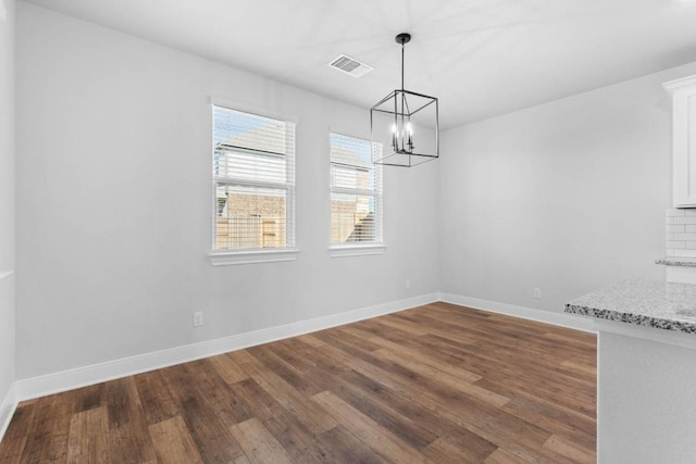 unfurnished dining area with dark wood-style floors, baseboards, visible vents, and a notable chandelier