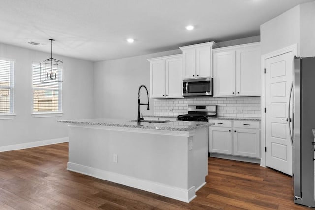 kitchen with pendant lighting, a center island with sink, appliances with stainless steel finishes, white cabinetry, and light stone countertops