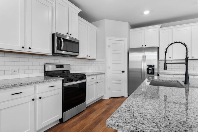 kitchen with light stone counters, dark wood finished floors, stainless steel appliances, white cabinets, and a sink