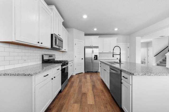 kitchen with white cabinets, light stone counters, stainless steel appliances, and a sink