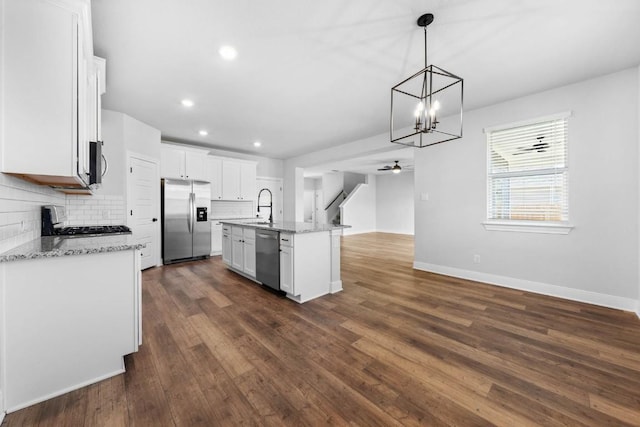 kitchen featuring a kitchen island with sink, white cabinetry, open floor plan, appliances with stainless steel finishes, and decorative light fixtures