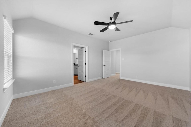 unfurnished bedroom featuring ensuite bathroom, light carpet, visible vents, baseboards, and vaulted ceiling