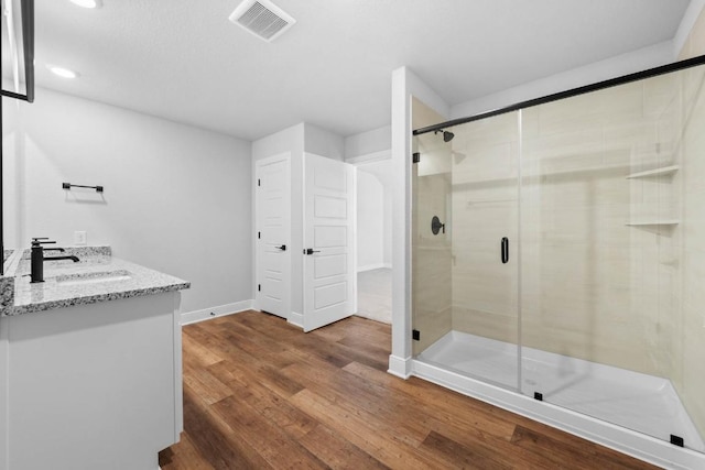 bathroom featuring visible vents, vanity, a shower stall, wood finished floors, and baseboards