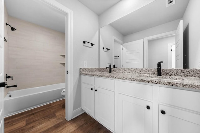 full bath featuring double vanity, visible vents, toilet, wood finished floors, and a sink