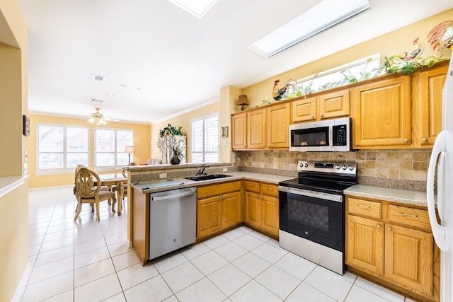 kitchen with stainless steel appliances, a peninsula, a sink, light countertops, and decorative backsplash