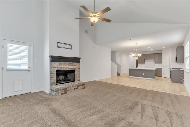 unfurnished living room with light carpet, visible vents, ceiling fan with notable chandelier, a brick fireplace, and recessed lighting