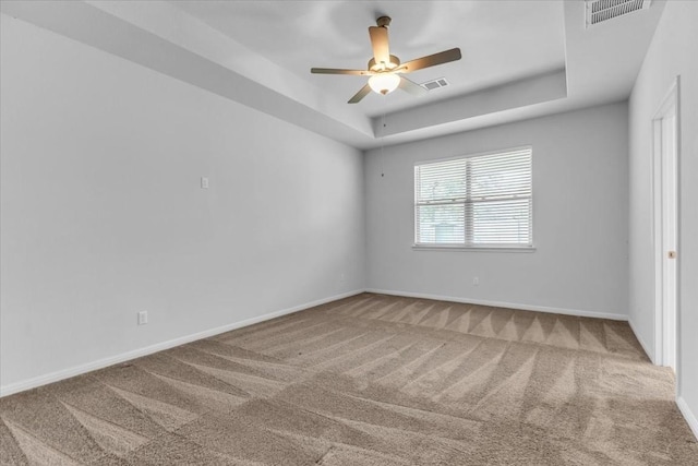 carpeted empty room with a tray ceiling, visible vents, and baseboards