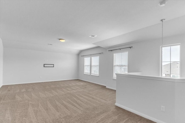 spare room with light carpet, vaulted ceiling, visible vents, and baseboards