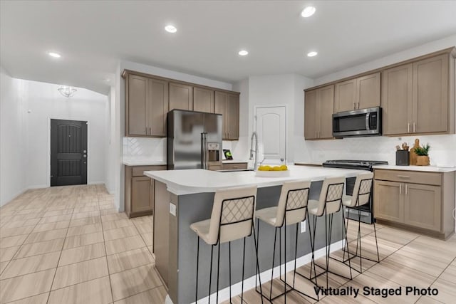 kitchen with a center island with sink, a sink, light countertops, appliances with stainless steel finishes, and a kitchen bar