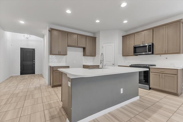 kitchen with stainless steel appliances, light countertops, a sink, and a center island with sink