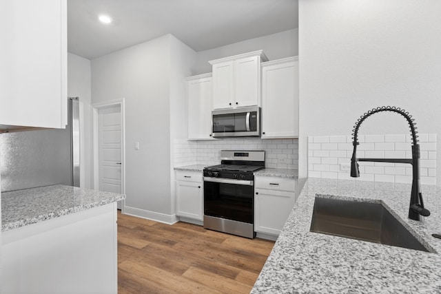 kitchen with stainless steel appliances, white cabinetry, a sink, and light stone counters